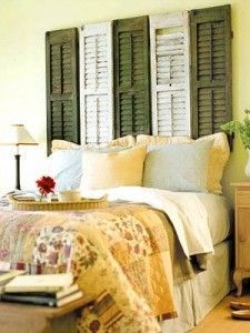Un dormitorio acogedor con una cama con edredón y varias almohadas, flanqueada por una mesita de noche con lámpara y cabeceros únicos hechos con contraventanas reutilizadas sobre un fondo amarillo claro.