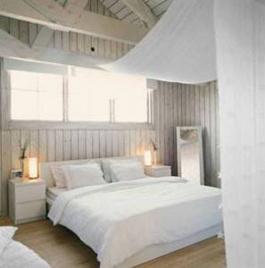 Una habitación serena con paredes blancas, un techo inclinado y una cama doble vestida en ropa de cama blanca flanqueada por dos meses.