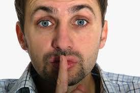 Un hombre de barba incipiente se lleva el dedo índice a los labios en un gesto de silencio, insinuando la reducción de ruido, con la mirada directa hacia la cámara.