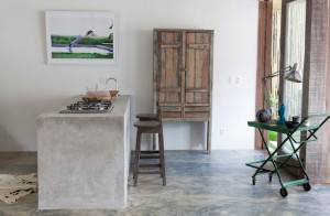 Una cocina minimalista con un suelo para cocina de hormigón, una isla de hormigón, una encimera de gas, un taburete de madera, un g