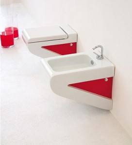 Un lavabo de baño moderno con diseño en blanco y rojo que presenta un lavabo angular montado sobre una pared blanca, acompañado de un grifo metálico, con elementos decorativos e inodoros rojos cerca.
