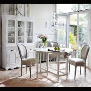 Un luminoso comedor con una mesa redonda blanca con dos sillas, un mueble blanco, suelo de terracota y grandes puertas de cristal que dan al exterior, desprende un ambiente romántico perfecto para el otoño.
