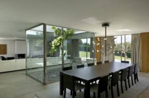 Una moderna sala de comedor con una gran mesa negra y sillas, que cuenta con un patio de luces con vegetación, y tiene vista a un césped al aire libre.