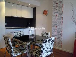 Una cocina-comedor moderna, al alcance de cualquiera, con una mesa de cristal, cuatro sillas con patrones florales en blanco y negro, armarios blancos,