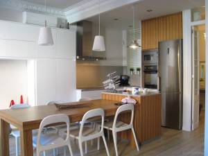 Una cocina moderna con mesa de comedor de madera, sillas blancas, electrodomésticos de acero inoxidable y reformas de precio medio del Plan Reforma.
