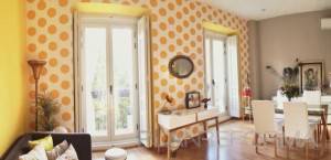 Una sala de comedor brillante y alegre con paredes blancas decoradas con grandes lunares amarillos, al estilo Kitsch, que cuenta con una mesa de comedor con