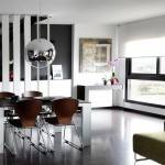 Una moderna sala de estar con paredes negras, que cuenta con un sofá verde, una zona de comedor con una mesa blanca y sillas marrones, y grandes ventilaciones.