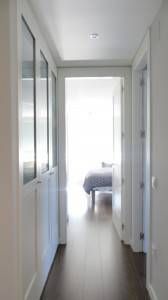 Un dormitorio muy iluminado visto al final de un pasillo sobreexpuesto con puertas abiertas a ambos lados, cortesía de una reforma integral de Espacio GO Majadahonda.