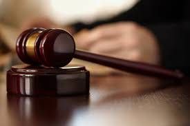 Mazo de madera sobre un escritorio con una persona borrosa al fondo, lo que sugiere un "dictamen pericial" o entorno judicial.