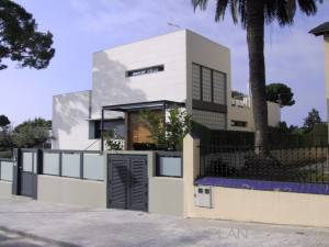 Moderna nueva casa de dos plantas con una fachada blanca, que muestra una combinación de paneles de madera, ventanas de bloque de vidrio y un techo plano.