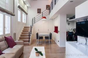 Interior de casa moderna con espacios en doble altura que incluye sala de estar, área de comedor y escaleras, presentando colores neutros, una lámpara de a