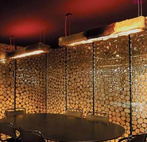Interior de una sala con mesa redonda y sillas, decorada con paredes de troncos de madera e iluminada por una cálida iluminación ambiental.