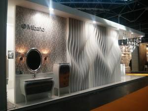 Un escaparate de baño moderno con un lavabo decorativo, un espejo ovalado y diseños de paredes texturizados inspirados en CEVISAMA.