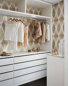 Una ordenada organización en el vestidor resaltando un diseño de papel pintado blanco y floral, con una variedad de ropa de colores pastel colgada en una barra.