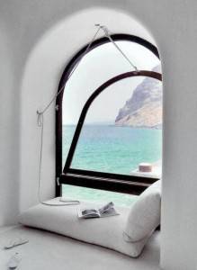 Ventana arqueada con vista al mar y al acantilado, con un asiento acolchado diseñado para el "día del libro 2014", un libro abierto y una lámpara colgante para decorar el