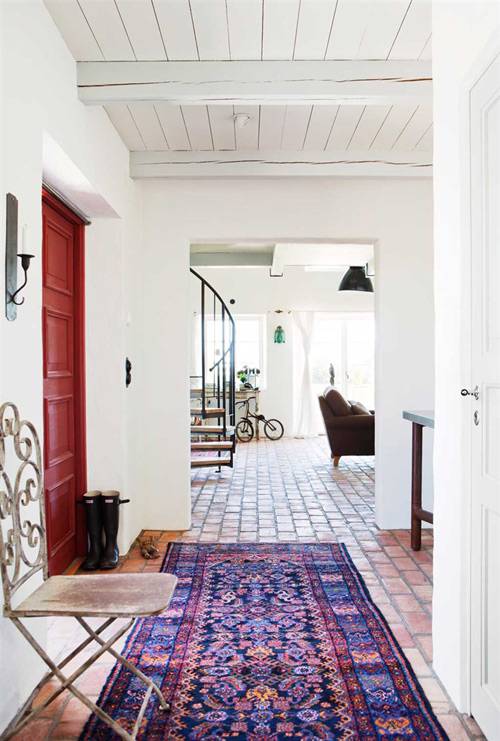 Entrada a la vivienda con el toque de color de la puerta roja y la alfombra de estampado azul y rojo tipo kilim.