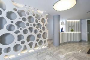 Una moderna área de recepción que presenta una partición decorativa perforada con formas circulares orgánicas, un elegante mostrador blanco y una persona contratada trabajando detrás del