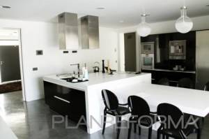 Cocina moderna con una isla central, taburetes de bar, luces colgantes y electrodomésticos de acero inoxidable.