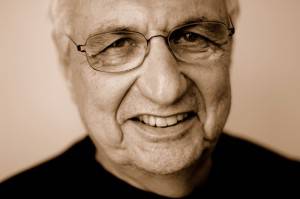 Primer plano retrato de un anciano sonriente, el arquitecto Frank Gehry, con gafas.