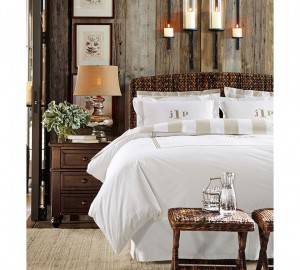 Una acogedora habitación con decoración de cama que incluye un gran lecho con juegos de sábanas blancas y rayadas apoyados en una pared rústica.