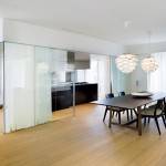 Una moderna sala de comedor con un suelo de madera, una mesa de comedor negra, sillas negras y luces colgantes únicas, adyacente a