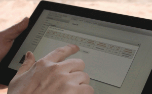 Una mano interactúa con una tableta digital, tocando un teclado en una pantalla para calcular estructuras.