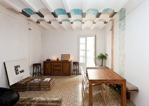 Una espaciosa habitación con decoración minimalista que cuenta con una mesa de madera y sillas, una alfombra estampada, un armario antiguo y elementos artísticos.