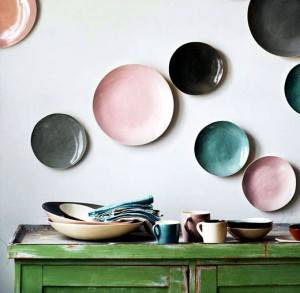 Una colección de platos y cuencos de cerámica en colores suaves se muestra en una pared y está arreglada sobre un aparato de madera verde, destac
