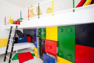 Una habitación infantil con una litera temática de Lego colorida, que cuenta con compartimentos de almacenamiento y un tobogán, incluyendo una escalera para acceder a