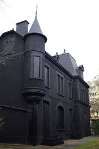 Un edificio pintado de negro que presenta decoración de Halloween y elementos arquitectónicos góticos, incluidas torres puntiagudas y ventanas estrechas, frente a un cielo nublado.