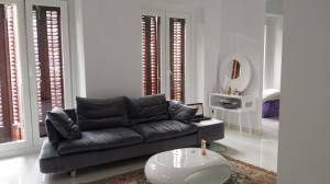 Una sala de estar moderna con un sofá seccional gris, paredes blancas y luz natural que se filtra a través de ventanas de listones de madera, diseñada por AGC arquitectos como parte de un proyecto de arquitecto.