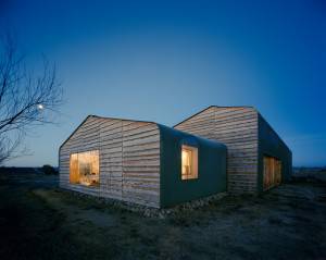 Una casa moderna, de diseño único, con revestimiento corrugado, iluminada desde dentro, se alza contra el cielo del atardecer como la Casa del año 2014.