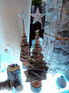 Dos adornos de árbol de Navidad de madera con estrellas en la parte superior se exhiben sobre una superficie, rodeados de otros artículos decorativos. Estos sig