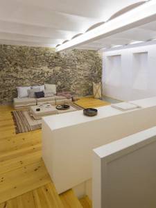 Los muebles y comodidades modernos se yuxtaponen con paredes rústicas de piedra vista en una habitación bien iluminada con piso de madera, que muestra la adaptación de Cotacero Taller de Arquitectura para vivienda.
