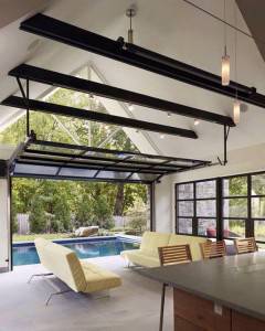 Una moderna sala de estar con claves de buena iluminación, techos altos con vigas expuestas de color negro, grandes ventanas con vistas a una piscina y muebles.