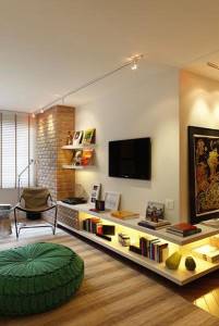 Una acogedora sala de estar moderna que presenta una pared de acento de ladrillo, iluminación para iluminar casa con rieles, televisión montada.