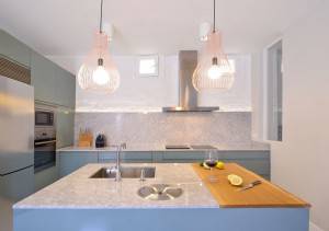Una cocina moderna con gabinetes azules, encimeras de mármol y una fantástica reforma en la iluminación colgante.