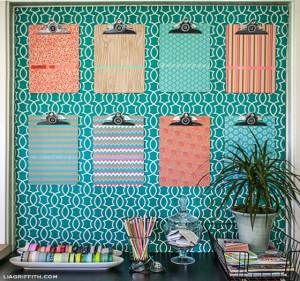 Una exhibición de pared organizada con portapapeles con varios patrones de papel, colocados sobre un escritorio con marcadores, lápices y una planta ornamental para ideas decorativas.