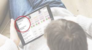 Una persona sentada con una tableta en la mano, mostrando lo que parece ser una interfaz de usuario para comparar presupuestos con datos e imágenes de perfil; una sección de la pantalla está rodeada de rojo.