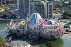 Un edificio de arquitectura moderna que se asemeja a una flor de loto situada al lado de un cuerpo de agua con un paisaje urbano circundante.