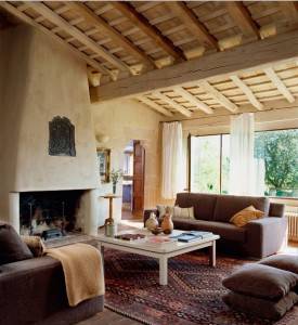 Una acogedora sala de estar decorada con estilo rústico, destacando una chimenea, vigas de madera a la vista, un sofá mullido y