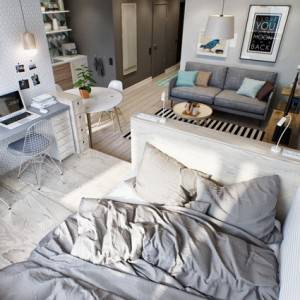 Moderno apartamento tipo estudio con una cama cuidadosamente hecha en primer plano y una cómoda sala de estar al fondo, diseñada para aprovechar el espacio. Cuenta con una pequeña cocina, un sofá azul y una cocina compacta.