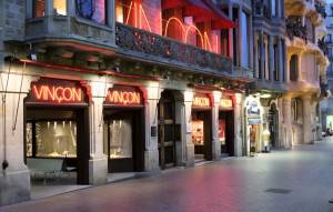 Una calle de la ciudad al atardecer con el escaparate de 'Galerías Vinçon' iluminado, con toldos rojos y escaparates.
