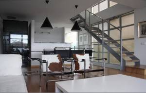 Una reforma integral ha transformado esta sala de estar moderna, ahora con un diseño minimalista que incluye un sofá blanco, una mesa de centro de cristal, sillas negras.