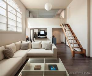 Una sala de estar moderna con una paleta de colores neutros con sofás beige, una mesa de centro de vidrio, pisos de madera y una escalera minimalista que conduce al nivel superior, con abundante luz natural que entra por grandes ventanales.