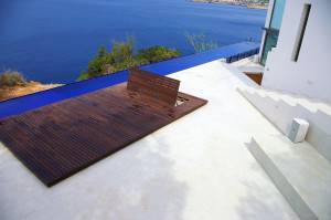 Una terraza moderna, reformada en el momento perfecto, con banco de madera y piscina infinita con vistas a la costa.