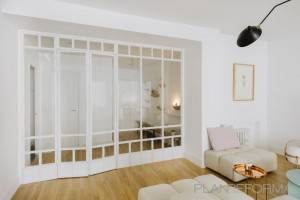 Una decoración brillante y minimalista en el salón con paredes blancas, destacando un sofá rosa claro, redondos otomanos beige, una mesa de centro redonda.