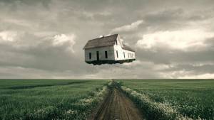 Una casa, ejemplificando el futuro de la arquitectura, parece estar flotando sobre un camino de tierra en un campo rural, con nubes grises en el fondo.