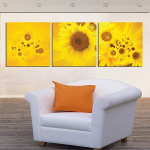 Un tríptico de decoración con tema de girasoles cuelga en una pared sobre un sillón blanco con un cojín naranja.