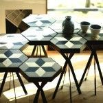 Una mesa modular con secciones hexagonales revestidas de baldosas hidráulicas en blanco y negro, luciendo un jarrón decorativo y dos tazas sobre su superf.